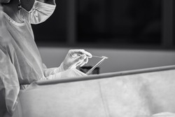 A surgeon wearing sterile gloves operates with a needle holder, a surgical needle and a surgical thread. Selective focus. Black and white photo.