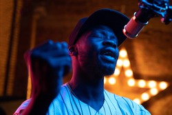 Man with beard and mustaches in baseball cap and t-shirt sing in microphone. Pink and blue neon light, star on background