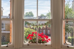 Interior of a Victorian British house with old wooden white windows  and red geraniums on the window sill facing a traditional English street
