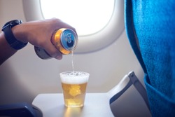 Male hand pouring beer into a plastic glass and making too much foam head on the airplane. Happy man drinking beer on airplane.