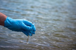 Water sample. A man's hand in a blue glove takes a sample water into a test tube. The concept of analysis of water purity, environmental pollution. Water testing for infections. Background, copy space
