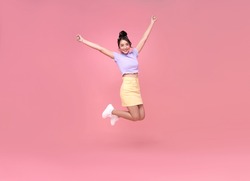 Happy Asian woman smiling and jumping while celebrating success isolated over pink background.