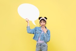 Excited Asian teen girl holding blank speech bubbles on yellow background.