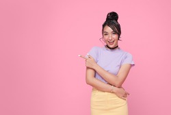 Happy young Asian teen woman standing with her finger pointing isolated on pink background with copy space. 
