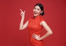 Happy Asian woman wearing traditional cheongsam qipao dress hand pointing up to copy space isolated on red background. Happy Chinese new year