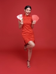 Happy Chinese new year. Asian woman wearing traditional cheongsam qipao dress holding angpao or red packet monetary gift isolated on red background.