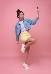 Happy young asian teen woman celebrating with mobile phone isolated over pink background.