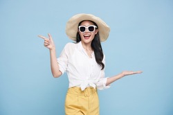 Young elegant beautiful Asian woman dressed in summer clothes smiling and pointing to empty copy space isolated on blue background.