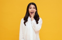 Amazed young Asian teen woman looking at camera on yellow background.