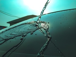 The glass of a car with water falling into a line, seen as many dripping water droplets in the mid-day sunlight.