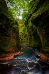 Inside of the Devil’s Pulpit gorge, with beautiful running water and red river bed with walk in the water towards a waterfall, near Glasgow, Scotland, UK