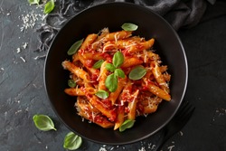 Penne pasta with tomato sauce, parmesan cheese and basil on dark background. Top view with copy space.