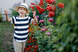 Cute little boy in a straw hat enjoying the flowers of a blooming garden, spring. Seasonal children's allergies. Concept of Mother's Day or International Women's Day