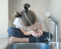 Healthy thirsty caucasian child drinking from water tap or faucet in kitchen. Hands open for drinking tap water. Pouring clean fresh drink. Concept of healthy lifestyle. Good habits. World Water Day