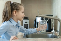 Little girl open a water tap with her hand holding a transparent glass. Kitchen faucet. Filling cup beverage. Pouring fresh drink. Hydration. Healthcare. Healthy lifestyle. World Water Day