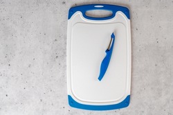 Plastic cutting board and vegetable peeler close-up, flat lay with copy space