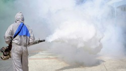 Rear view of outdoor healthcare worker in protective clothing using fogging machine spraying chemical to eliminate mosquitoes and prevent dengue fever at general location in community