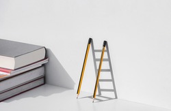 Two pencils and shadow in form of ladder with stack of textbooks on white tabletop, Education, learning is the ladder to success concept. 