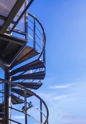 Low angle view of black metal spiral staircase outside of modern house building against blue sky in vertical frame 