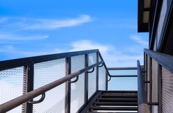 Low angle view of black metal staircase with handrail outside house against blue sky background