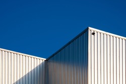 Corrugated Steel Warehouse Wall of Industrial Building against blue clear sky Background with light reflection on surface