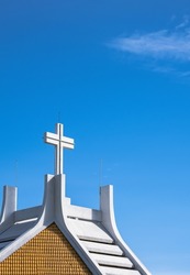 Large cross on top of white church against blue sky background in vertical frame