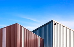 Low angle view of 2 modern brown and silver corrugated steel industrial building against blue sky background