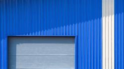 Automatic Roller Shutter Door and white stripe on Blue Corrugated Metal Wall of Warehouse Building