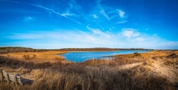 Coastal wildlife animal and seabird sanctuary lagoon with a wooden bench on the hill covered with golden grasses. Beautiful Cape Cod scenery in winter along the South Cape Beach.