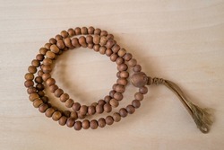 A circular brown bead necklace on the wooden table background. The necklace has the symbol of Buddhism and a bundle of the skein.