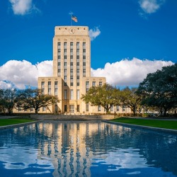 Houston City Hall building skyline, waving American Flags, and live oak trees with water reflections on the Herman Square water fountain in Texas, USA