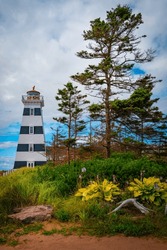 West Point Lighthouse park entrance with flowers, tall pine trees, and sign in O'Leary, Prince Edward Island, Canada
