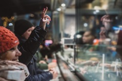 Person ordering a fresh kebab or gyros in a fast food stall or vendor outside in a city. Visible hands showing V sign to order food over the counter in festive evening.