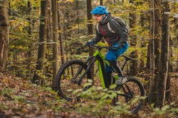 Biker riding uphill with a modern electric bicycle or mountain bike in autumn or winter setting in a forest. Modern e-cyclist in woods.