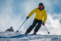 Young person in fashionable clothes is skiing towards the camera on a ski slope on a sunny day. Carve or carving on ski piste, perfect weather, strong backlight.