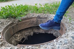 A man's foot is on an open sewer hatch, Danger concept city.