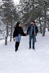 Walking of young lovers on valentine's day in winter forest on snow . Girl holds a red rose and a young handsome man. A young couple that wear outdoor clothes, looks very romantic to each other.