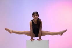 child athlete gymnast performing gymnastic exercise on top of apparatus, training for competition, colored background in a studio