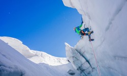 Epic shot of an ice climber climbing on a wall of ice. Mountaineer, climber or alpinist on an adventure extreme ascent with ice axe and crampons. Alpine extreme climbing on a serac or creavasse.