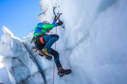 Epic shot of an ice climber climbing on a wall of ice. Mountaineer, climber or alpinist on an adventure extreme ascent with ice axe and crampons. Alpine extreme climbing on a serac or crevasse.