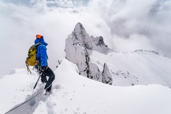 An alpinist climbing an alpine ridge in winter extreme conditions. Adventure ascent of alpine peak in snow and on rocks. Climber ascent to the summit. Winter ice and snow climbing in mountains.
