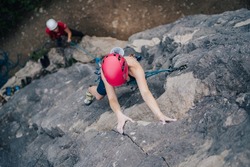 A climber climbing a rock. Woman climber rock climbing steep wall. Adventure sport activity, adrenaline. Girl climbing with a rope, helmet and other rock climbing equipment.