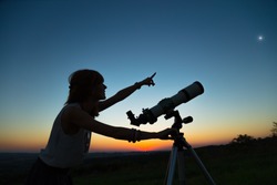 Young woman looking at the sky with a astronomical telescope.