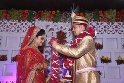 Bride and groom putting garland as a ceremonial proceeding as per Hindu Marriage Rituals and posing for the photograph. The Garland and is made of roses and white flower buds