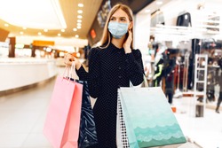 beautiful elegant young woman in a medical protective mask on her face, with shopping bags, walks through the shopping center