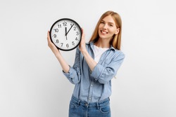 Happy young woman in casual clothes holding clock over isolated white background