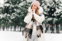 Portrait of a winter woman in warm clothes, Woman breathes on her arms to keep them warm on a cold winter day, Beautiful young woman outdoors. Cold weather concept, frozen hands
