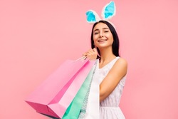 Beautiful woman in rabbit ears with shopping bags in her hands, spring shopping, a traditional holiday, in the studio on a pink background, Easter mood