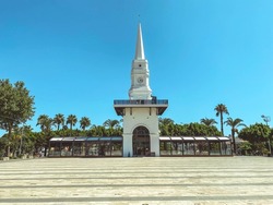 building spire in a tropical, hot country. white, high, sharp spire on the roof. a building with a tower at the top against the background of the sky, palm trees and greenery.