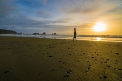 Adventurous athletic woman doing a handstand on Pacific Northwest beach during a beautiful sunset.